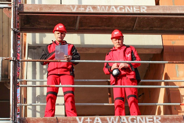 zwei Männer stehen auf einem Baugerüst, halten ein Weinglas in der Hand und sprechen einen Richtspruch