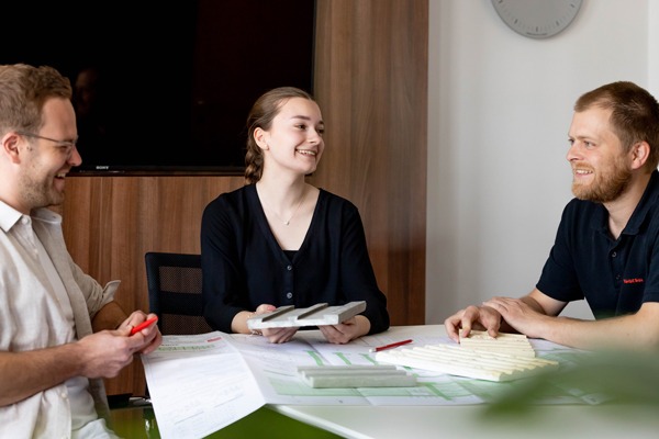 drei Personen sitzen in einem Besprechungsraum