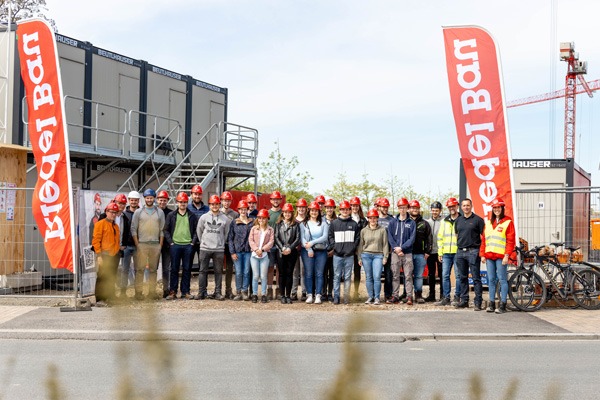 Gruppenaufnahme mit Bauhelmen vor Baucontainern mit zwei groeßen roten Beachflags