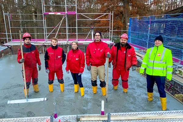 Sechs Personen betonieren eine Fläche in Arbeitskleidung