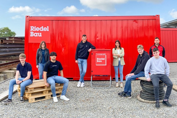 Ausbildungsstart 2021 - 8 Personen stehen vor einem roten Baucontainer