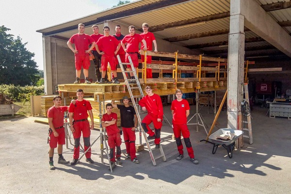 12 Personen stehen in roter Arbeitskleidung für ein Gruppenbild zusammen