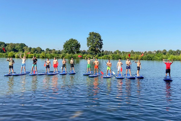 14 Personen stehen auf einem Stand up Paddel Board auf dem See